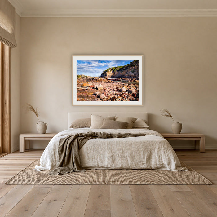 Lennards Island framed print in oak with a white mat, above an oatmeal linen bed in a bedroom