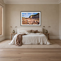 Lennards Island framed print in black with a white mat, above an ivory linen bed in a bedroom