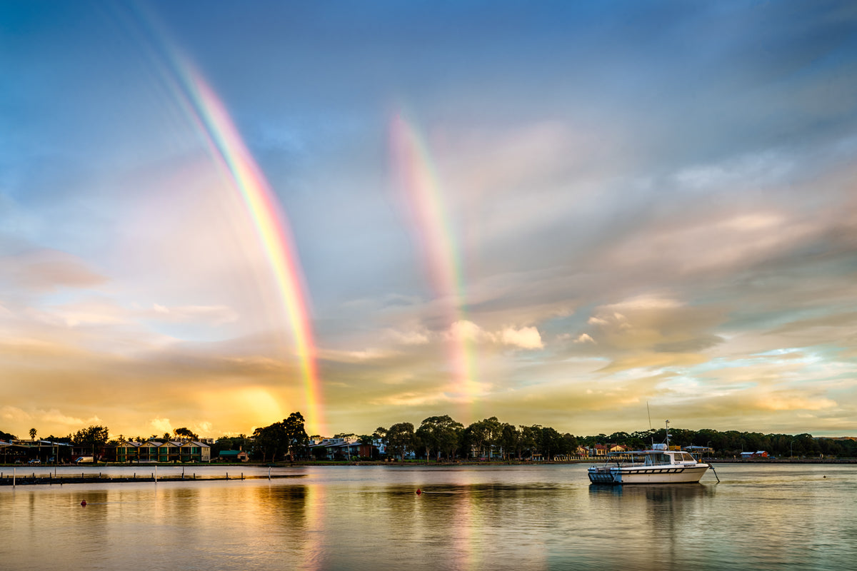 A double rainbow over Merimbula Lake at dusk, seen from the front of the Lakeview Hotel, with a boat at anchor — fine art print