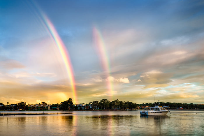 A double rainbow over Merimbula Lake at dusk, seen from the front of the Lakeview Hotel, with a boat at anchor — fine art print