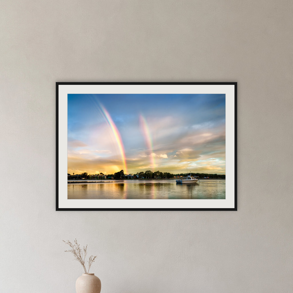Rainbow over Merimbula Lake framed print in black with a white mat, in a hallway