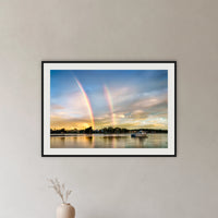Rainbow over Merimbula Lake framed print in black with a white mat, in a hallway