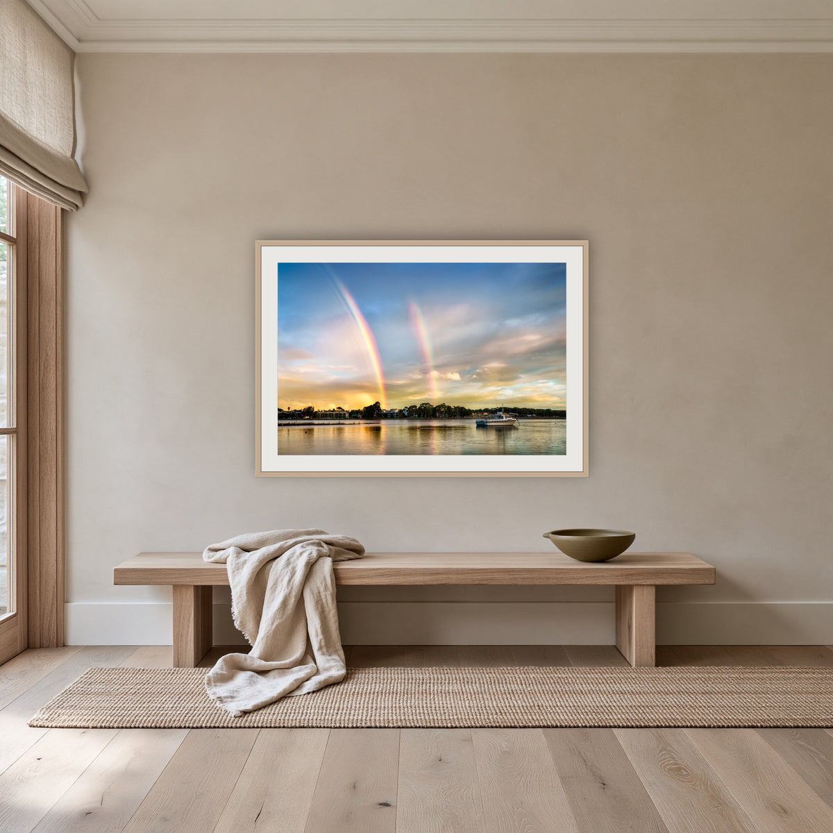 Rainbow over Merimbula Lake framed print in oak with a white mat, above an oak bench in a hallway