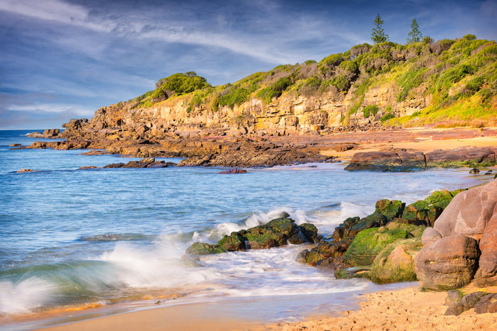 Golden light on the layered sandstone cliffs at Short Point, Merimbula, pines standing on the skyline and surf washing silk-smooth over green mossy rocks — fine art print