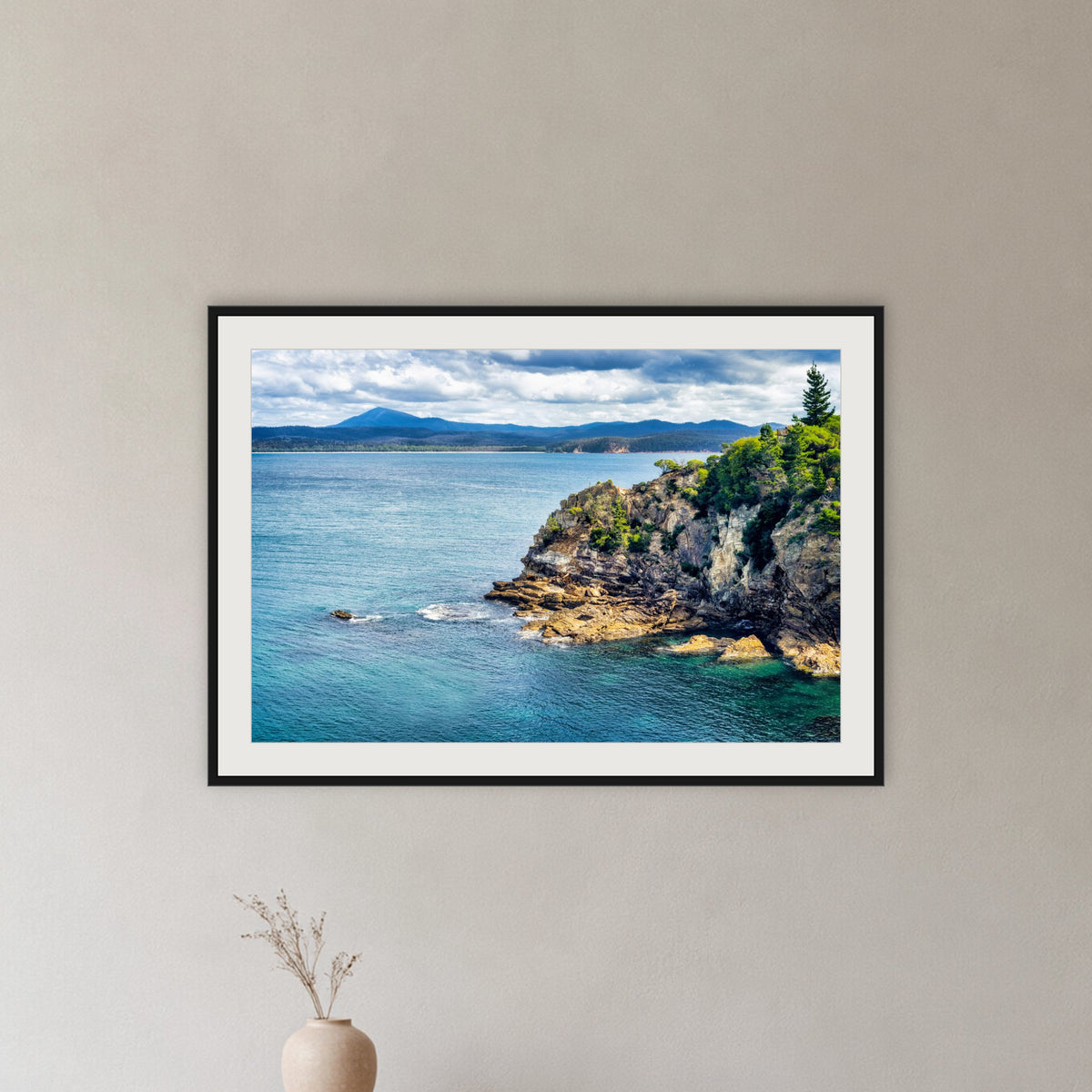 Twofold Bay Rocky Cliffs & Mt Imlay framed print in black with a white mat, in a hallway