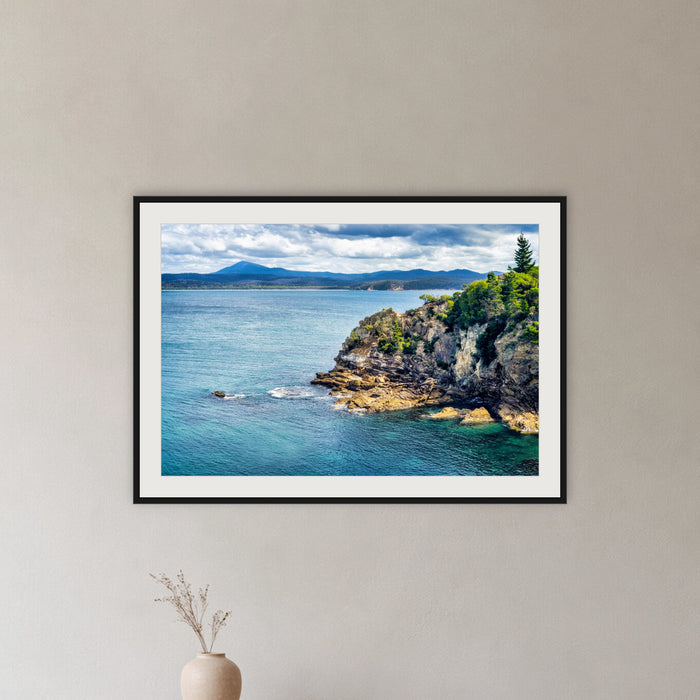 Twofold Bay Rocky Cliffs & Mt Imlay framed print in black with a white mat, in a hallway