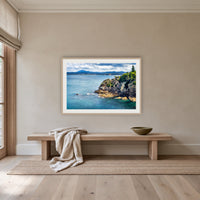 Twofold Bay Rocky Cliffs & Mt Imlay framed print in oak with a white mat, above an oak bench in a hallway