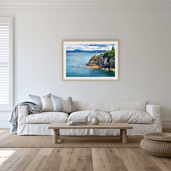 Twofold Bay Rocky Cliffs & Mt Imlay framed print in oak with a white mat, in a lounge room