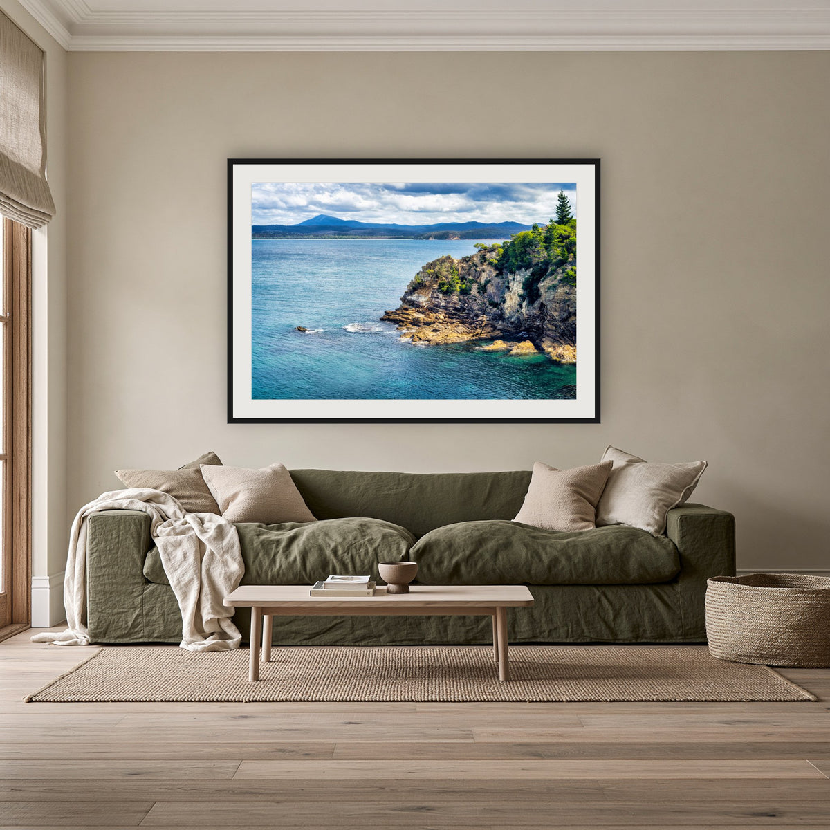 Twofold Bay Rocky Cliffs & Mt Imlay framed print in black with a white mat, above an olive linen sofa in a lounge room