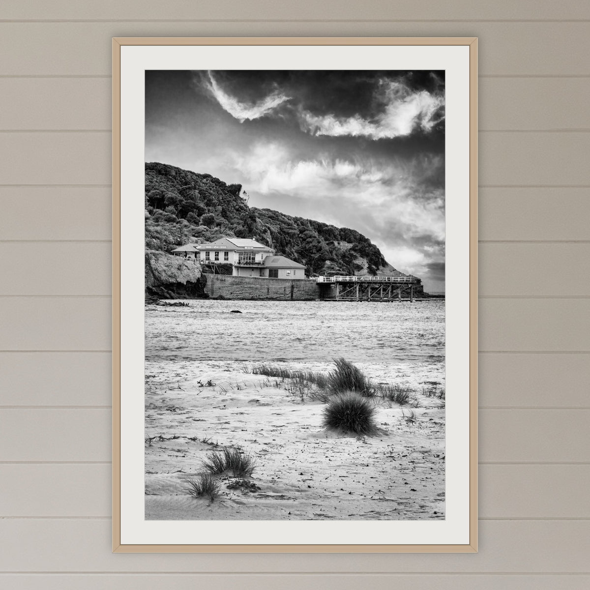 Merimbula Wharf from Main Beach in black and white, framed print in oak with a white mat, on a coastal lounge room wall