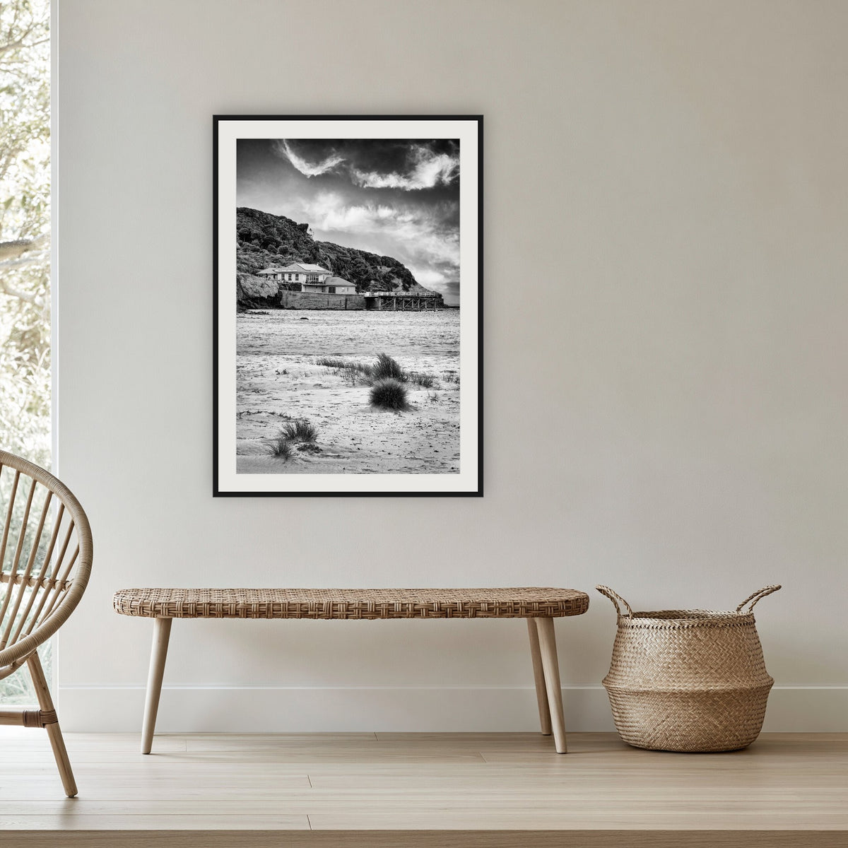Merimbula Wharf from Main Beach in black and white, framed print in black with a white mat, in a cane-panelled hallway