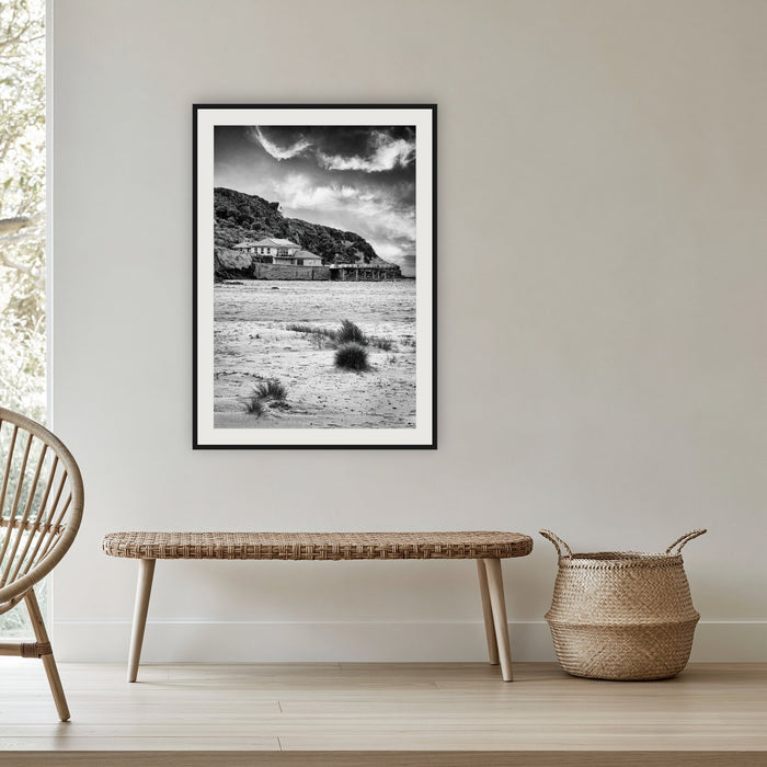Merimbula Wharf from Main Beach in black and white, framed print in black with a white mat, in a cane-panelled hallway