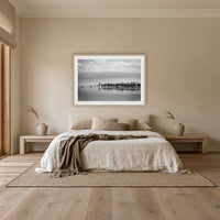 Mitchies Jetty in black and white with colour, framed print in oak with a white mat, above an oatmeal linen bed in a bedroom