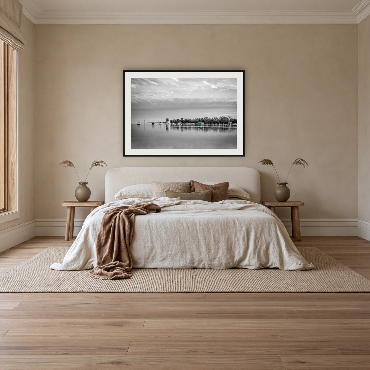Mitchies Jetty in black and white with colour, framed print in black with a white mat, above an ivory linen bed in a bedroom