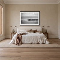 Mitchies Jetty in black and white with colour, framed print in black with a white mat, above an ivory linen bed in a bedroom