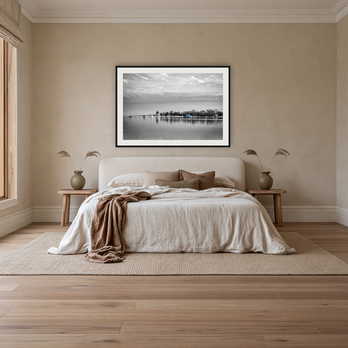 Mitchies Jetty in black and white with colour, framed print in black with a white mat, above an ivory linen bed in a bedroom