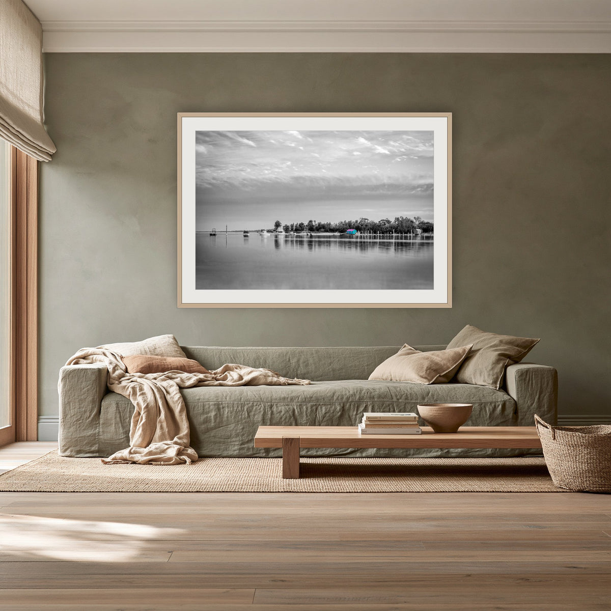 Mitchies Jetty in black and white with colour, framed print in oak with a white mat, above a sage linen sofa in a lounge room