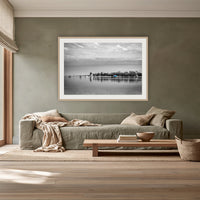 Mitchies Jetty in black and white with colour, framed print in oak with a white mat, above a sage linen sofa in a lounge room