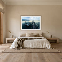 Little Boat at Fishpen Jetty framed print in oak with a white mat, above an oatmeal linen bed in a bedroom