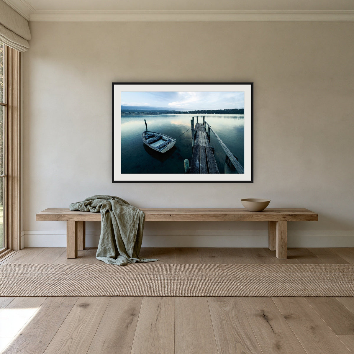 Little Boat at Fishpen Jetty framed print in black with a white mat, above an oak bench in a hallway