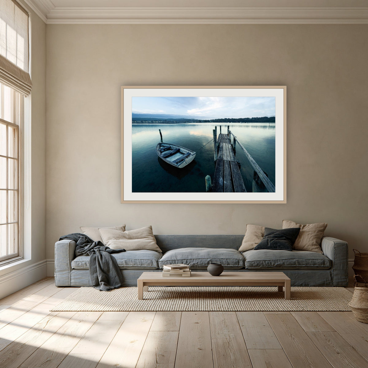 Little Boat at Fishpen Jetty framed print in oak with a white mat, above a dusty blue linen sofa in a lounge room