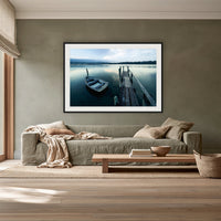 Little Boat at Fishpen Jetty framed print in black with a white mat, above a sage linen sofa in a lounge room