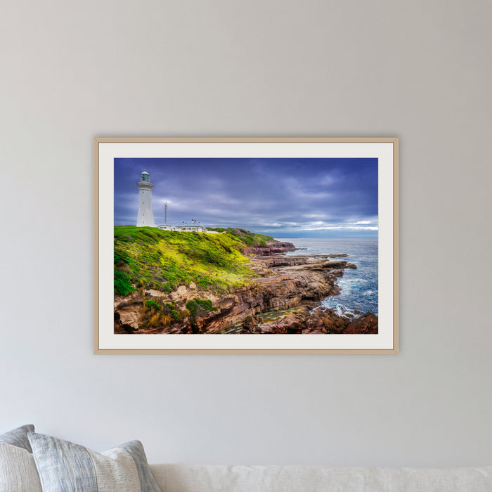 Green Cape Lighthouse framed print in oak with a white mat, in a lounge room