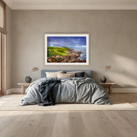 Green Cape Lighthouse framed print in oak with a white mat, above a dusty blue linen bed in a bedroom
