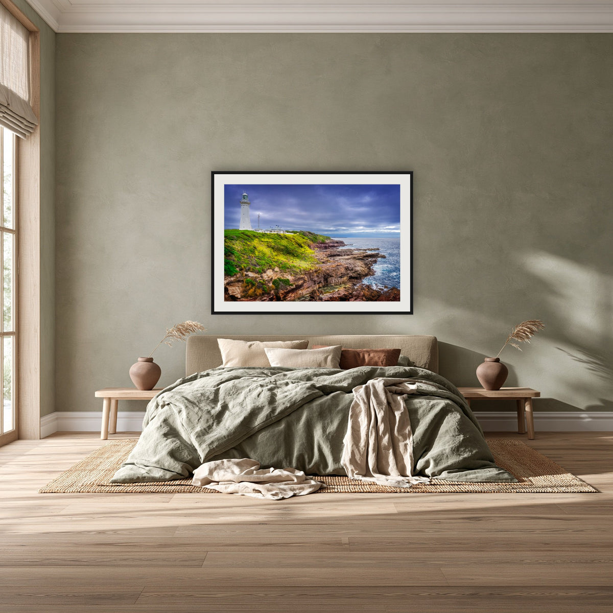 Green Cape Lighthouse framed print in black with a white mat, above a khaki linen bed against a green-grey wall in a bedroom