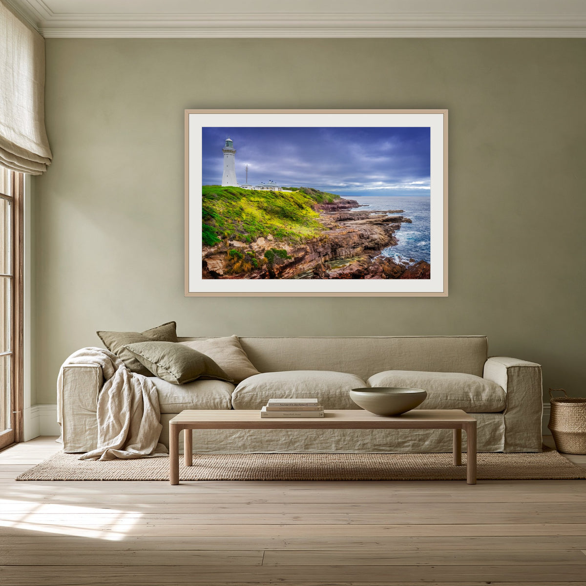 Green Cape Lighthouse framed print in oak with a white mat, above a linen sofa against a sage wall in a lounge room
