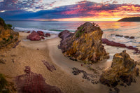 A glorious sunrise over Pambula Beach, magenta and violet cloud breaking to gold along the horizon, the light catching a tall rock outcrop while a channel of wet sand curves out to the sea — fine art print