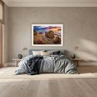 Pambula Beach Sunrise framed print in oak with a white mat, above a dusty blue linen bed in a bedroom