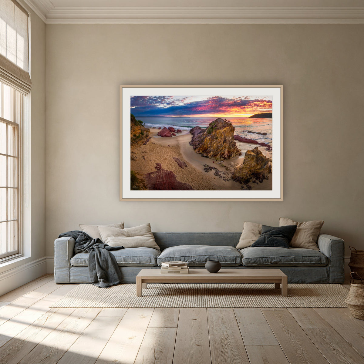 Pambula Beach Sunrise framed print in oak with a white mat, above a dusty blue linen sofa in a lounge room