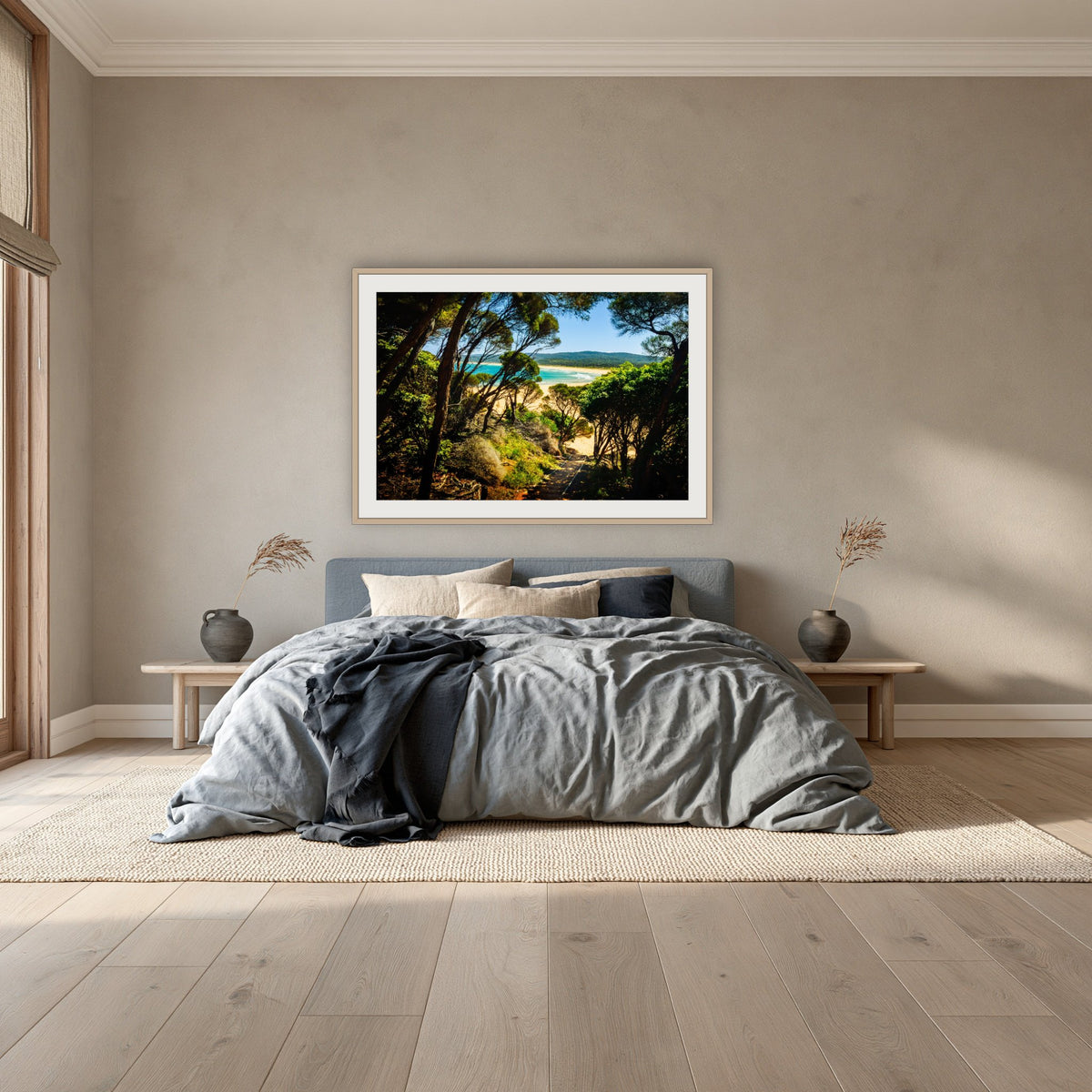 Wallagoot Lake framed print in oak with a white mat, above a dusty blue linen bed in a bedroom