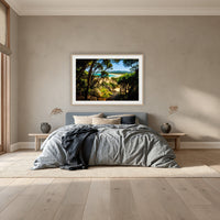 Wallagoot Lake framed print in oak with a white mat, above a dusty blue linen bed in a bedroom