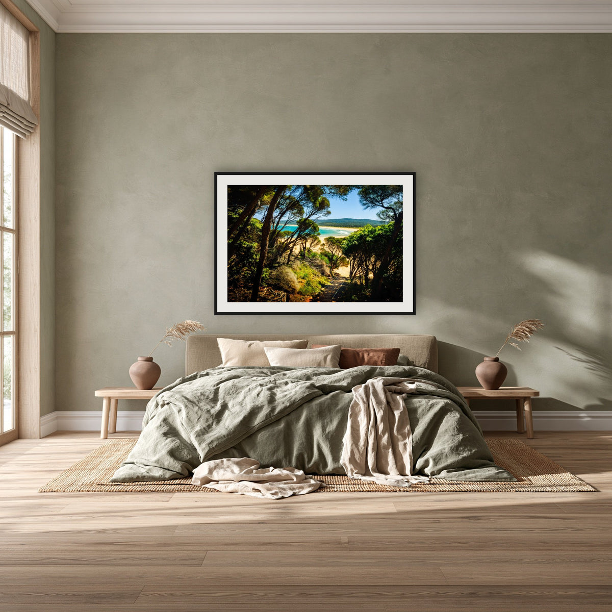 Wallagoot Lake framed print in black with a white mat, above a khaki linen bed against a green-grey wall in a bedroom