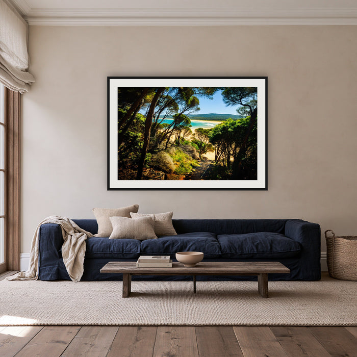 Wallagoot Lake framed print in black with a white mat, above a navy linen sofa in a lounge room