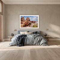 Pambula Rocks framed print in oak with a white mat, above a dusty blue linen bed in a bedroom