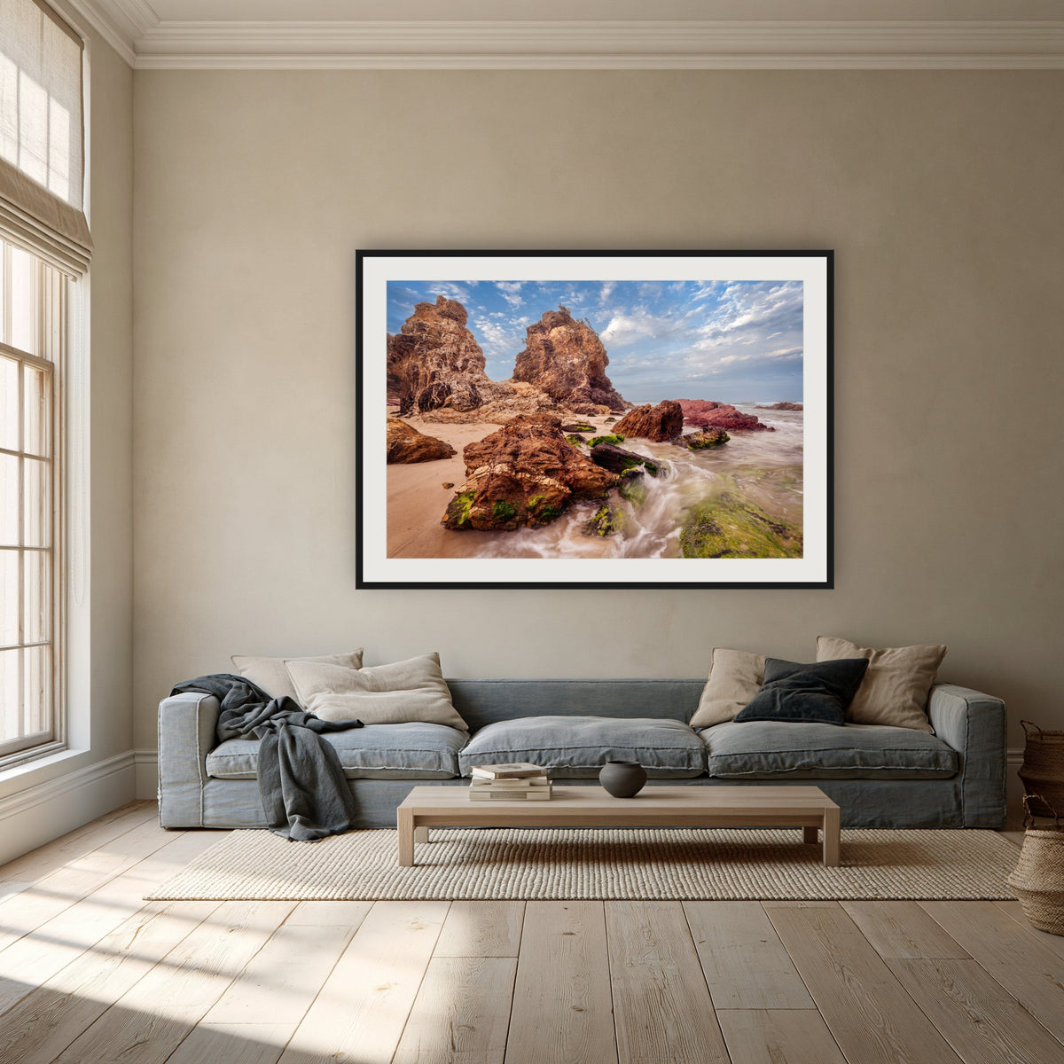 Pambula Rocks framed print in black with a white mat, above a dusty blue linen sofa in a lounge room