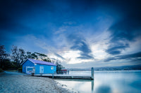 The blue boatshed at Mitchies Jetty reflected in the still waters of Merimbula Lake at dusk — fine art print