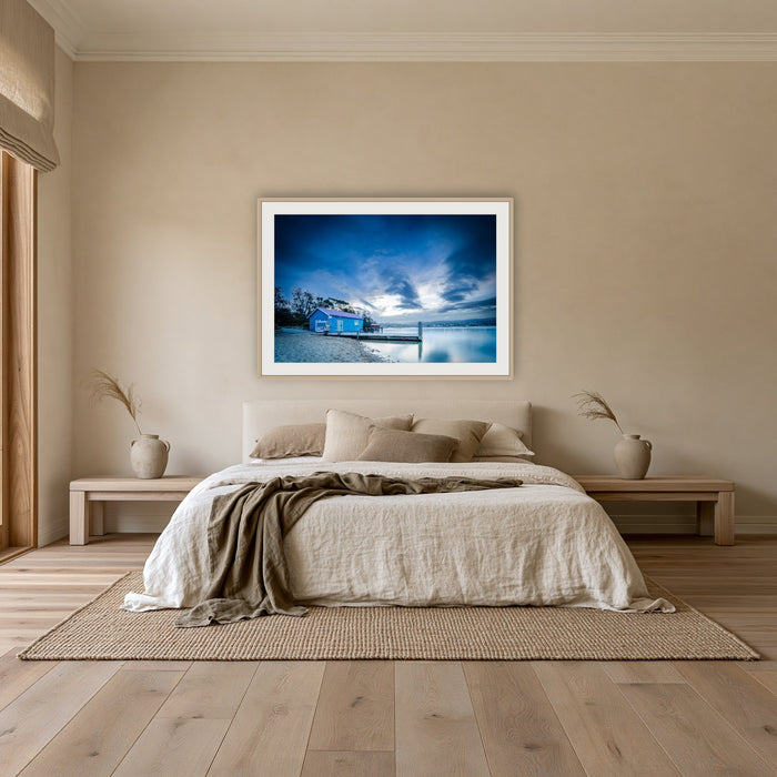 Mitchies Jetty at Dusk framed print in oak with a white mat, above an oatmeal linen bed in a bedroom