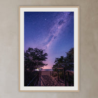 Main Beach Milky Way framed print in oak with a white mat, in a plaster-walled hallway