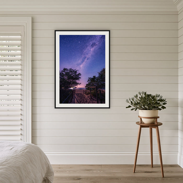 Main Beach Milky Way framed print in black with a white mat, in a coastal bedroom
