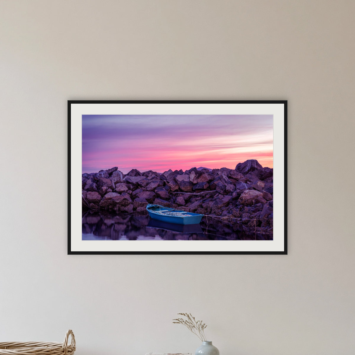 Eden Twofold Hush wall art — a lone blue dinghy against the Eden breakwall at last light, shown in a black frame with a mat in a hallway