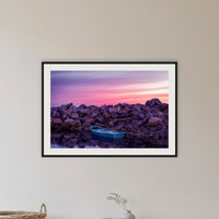 Eden Twofold Hush wall art — a lone blue dinghy against the Eden breakwall at last light, shown in a black frame with a mat in a hallway