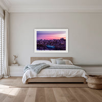 Eden Twofold Hush wall art — a lone blue dinghy against the Eden breakwall at last light, shown in a white frame with a mat in a bedroom