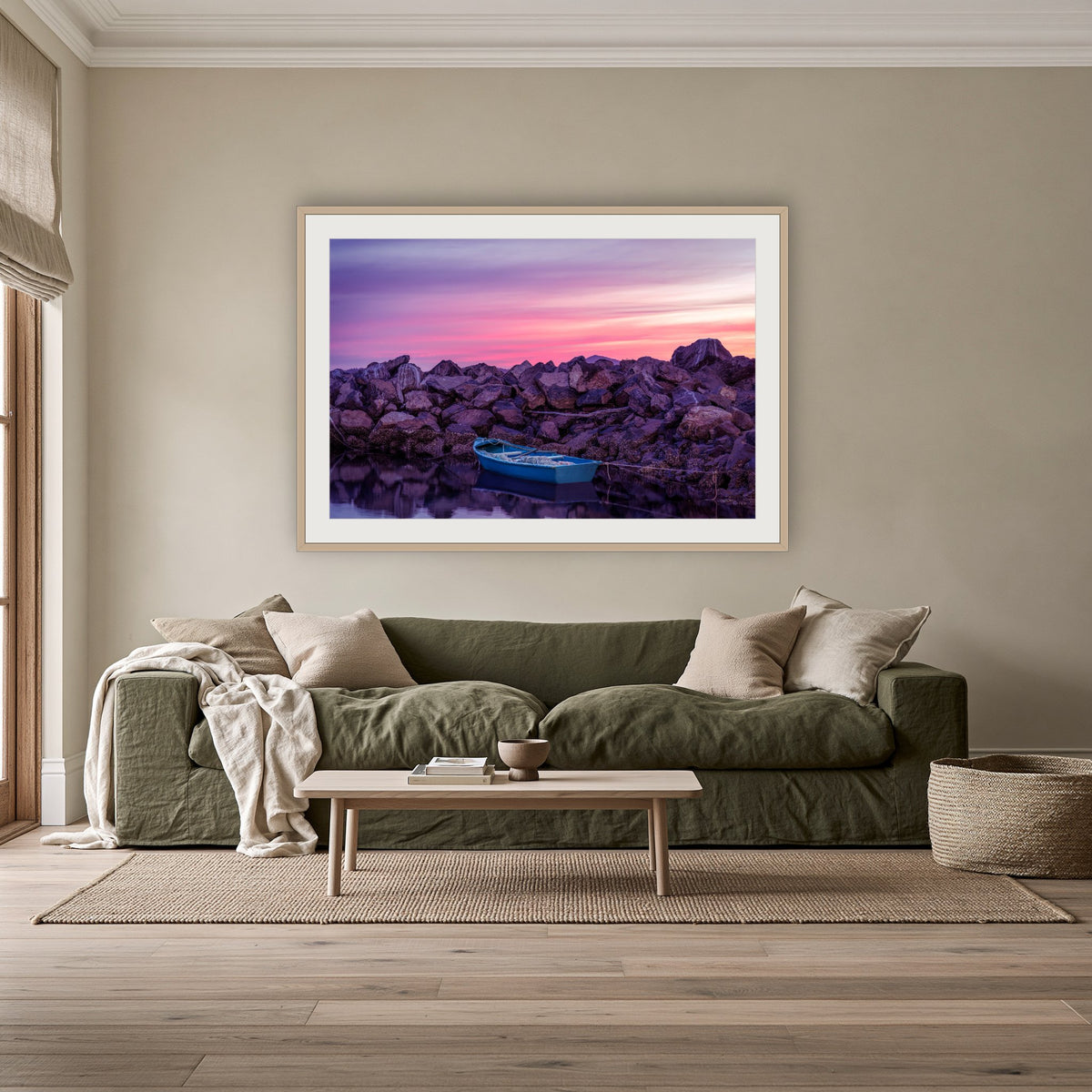 Eden Twofold Hush wall art — a lone blue dinghy against the Eden breakwall at last light, shown in an oak frame with a white mat above an olive linen sofa in a lounge room