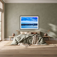 Dawn over Merimbula Lake framed print in black with a white mat, above a khaki linen bed against a green-grey wall in a bedroom