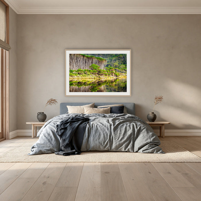 Bournda Lagoon's Serenity framed print in oak with a white mat, above a dusty blue linen bed in a bedroom