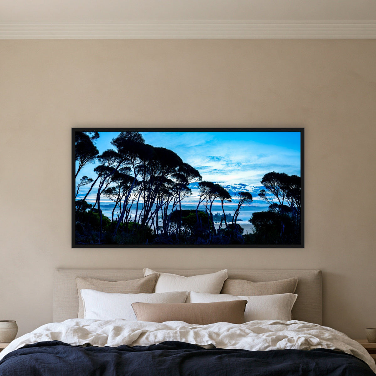 Wallagoot Lake and Sea at Blue Hour framed print in black without a mat, above a bed with a navy linen quilt in a bedroom
